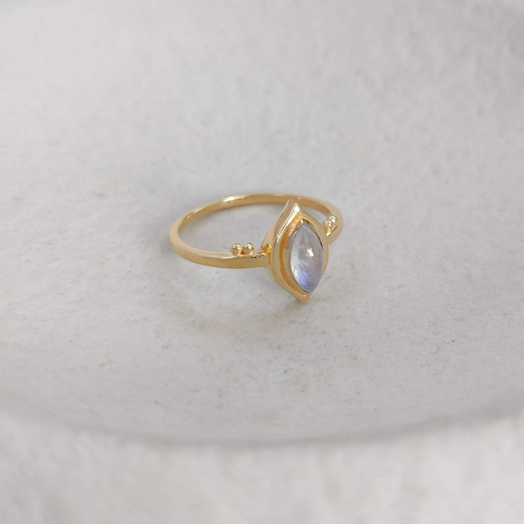 Gold ring with a marquise-shaped gemstone on a white surface.