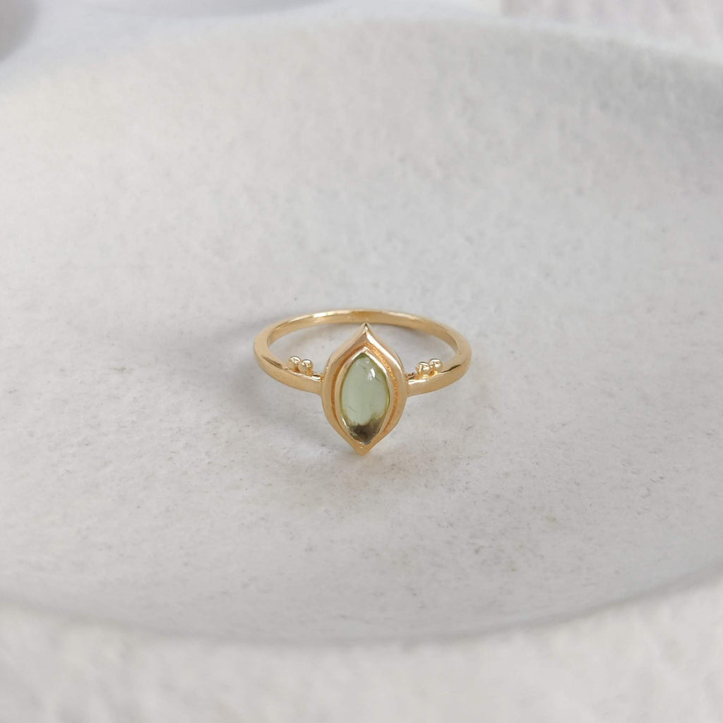 Gold ring with a green gemstone on a white stone surface.