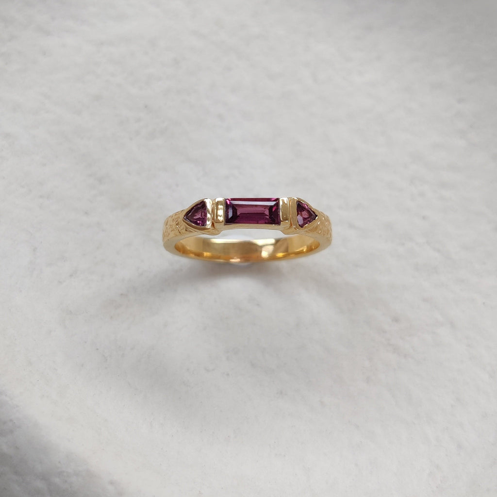 Gold ring with red purple gemstones on a textured white surface
