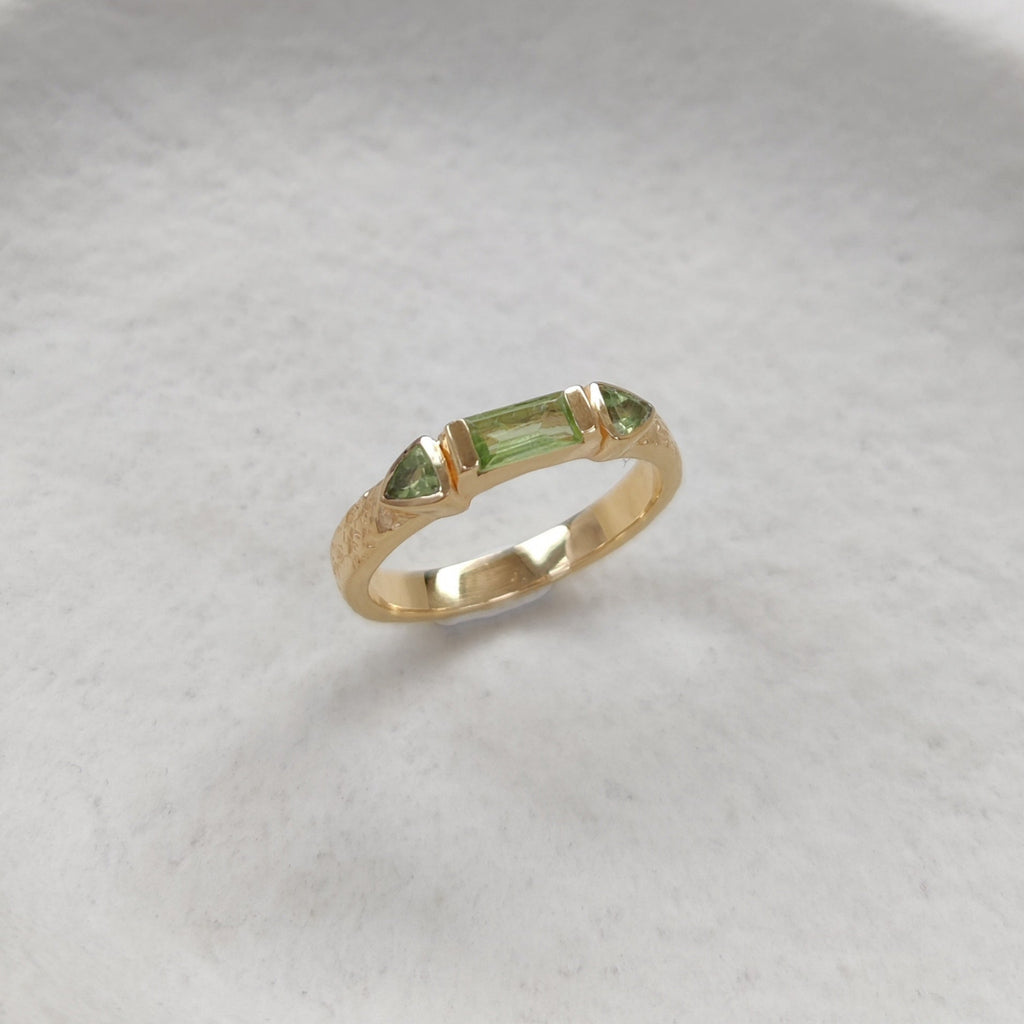 Gold ring with green gemstones on a textured white surface