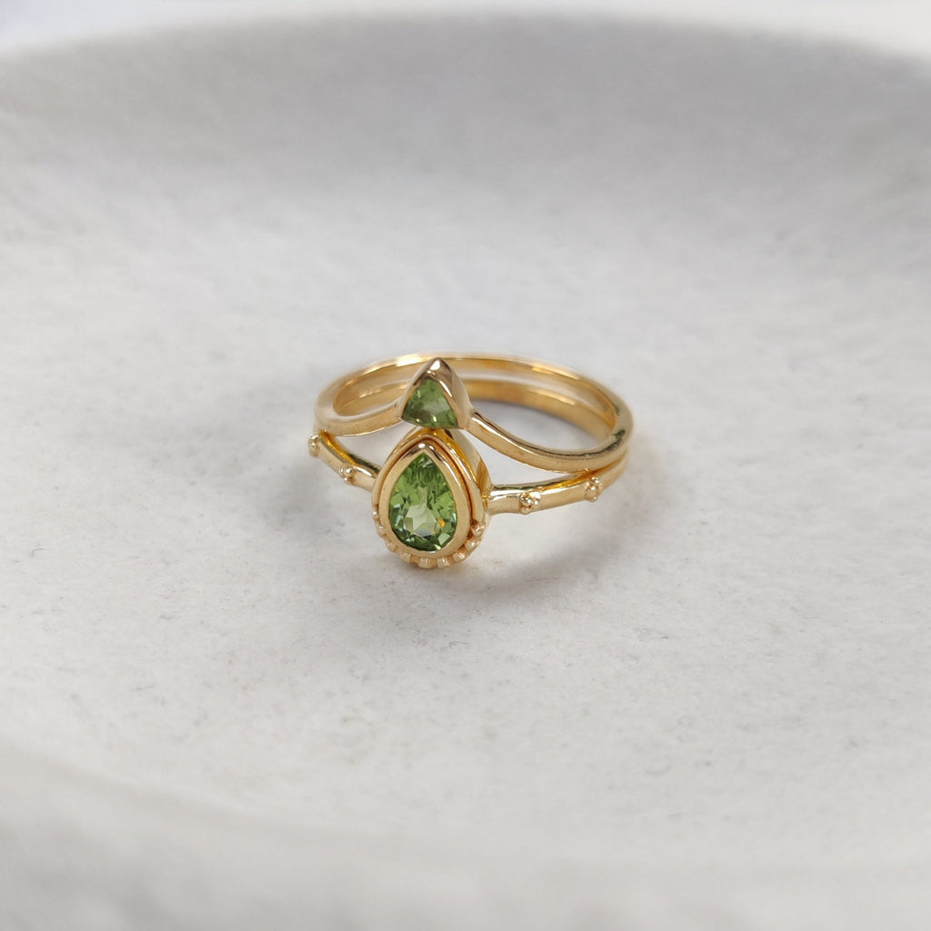Two gold stacking rings with green gemstones on a white background.