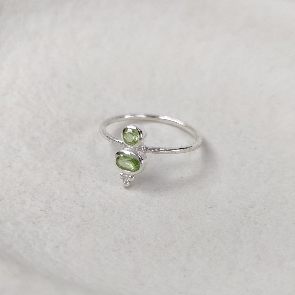 Silver ring with green gemstones on a white surface.