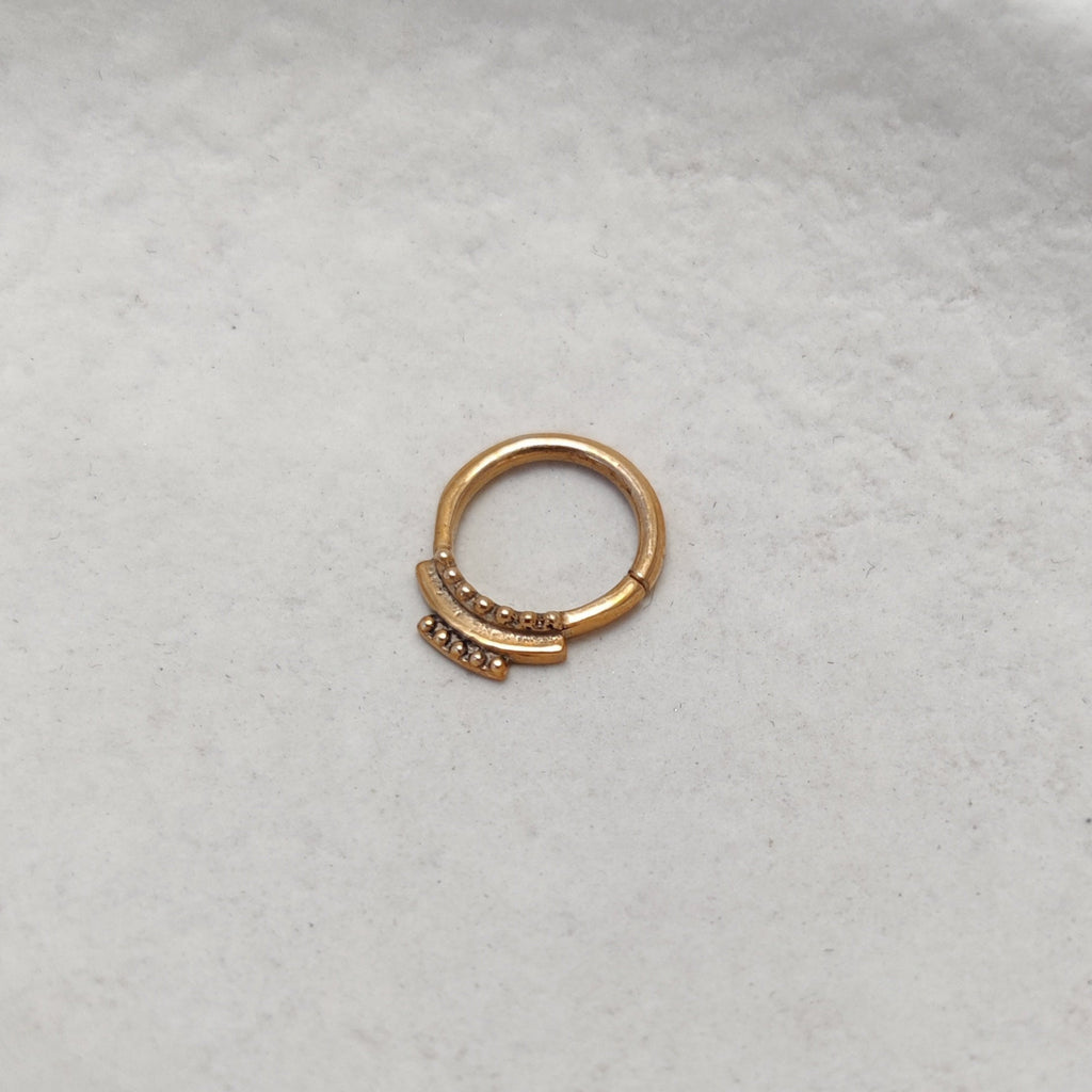 Dainty gold septum, side angle, on plain background.