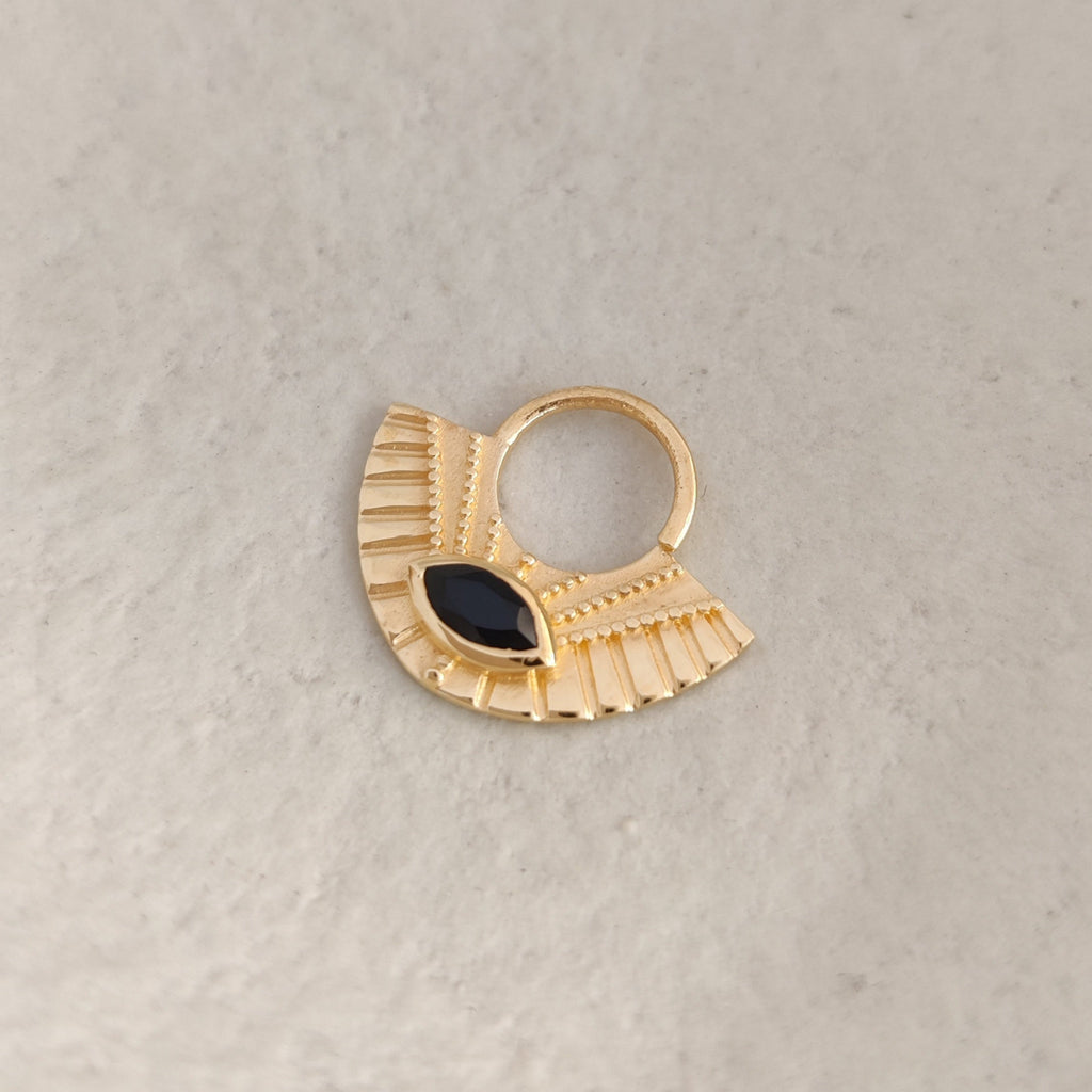 Gold septum nose ring with a black gemstone on a light background.