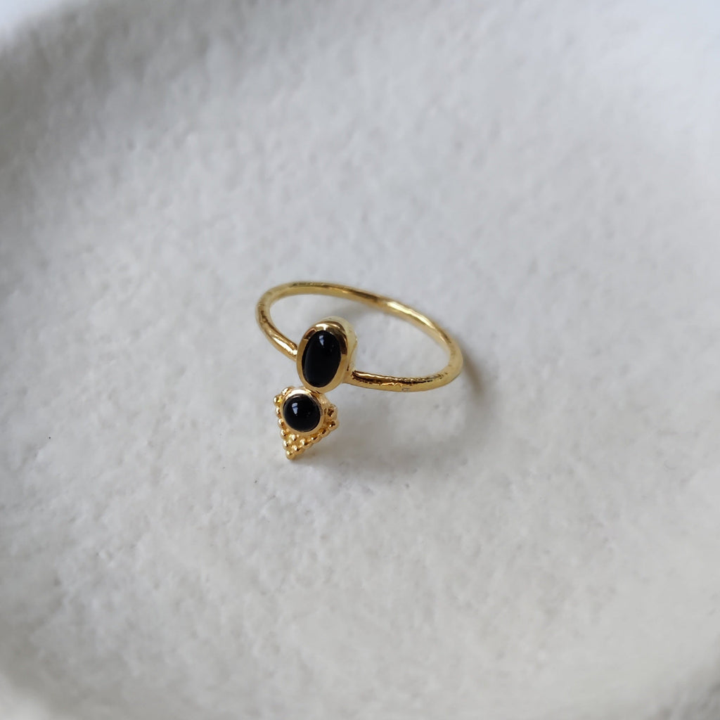 Dainty brass ring with black onyx, displayed on a jewelry plate.