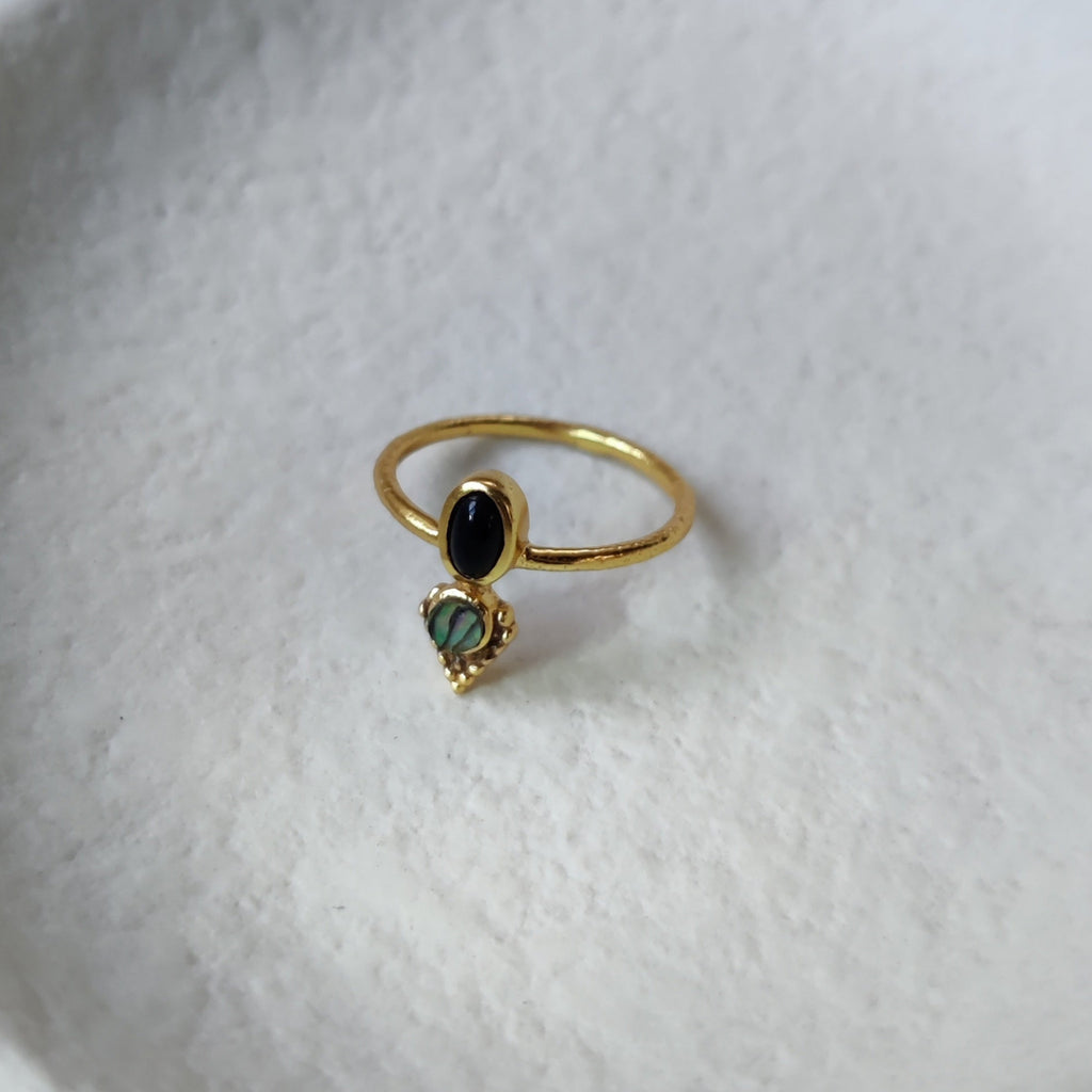 Dainty brass ring with black onyx and abalone shell, displayed on a jewelry plate.