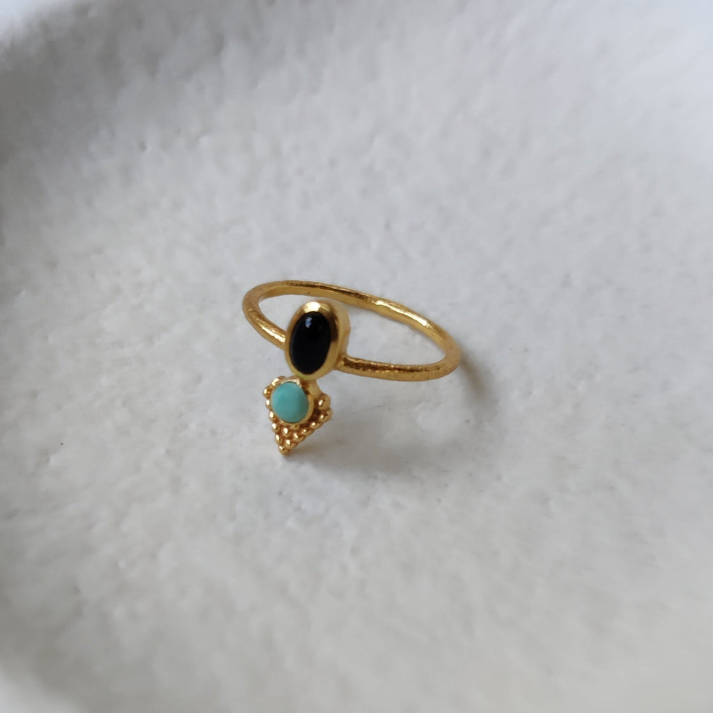 Dainty brass ring with black onyx and turquoise, displayed on a jewelry plate.