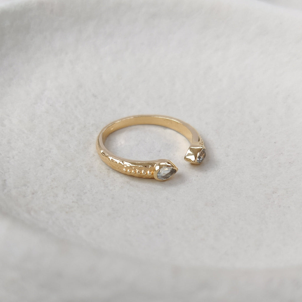 Gold ring with a open cuff design with two pear-shaped gemstones on a textured white surface.