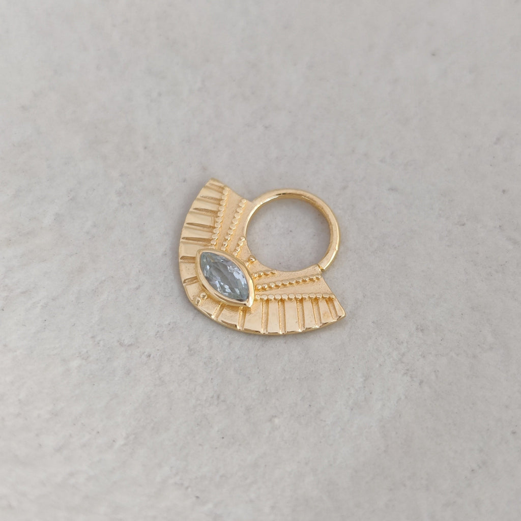 Gold septum nose ring with a gemstone on a light background.