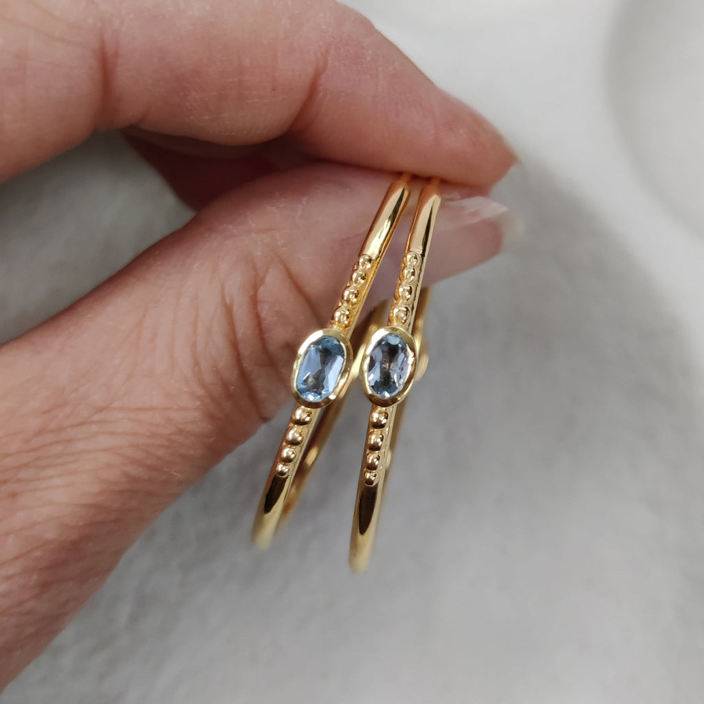Gold earrings with gemstones held by a hand against a neutral background