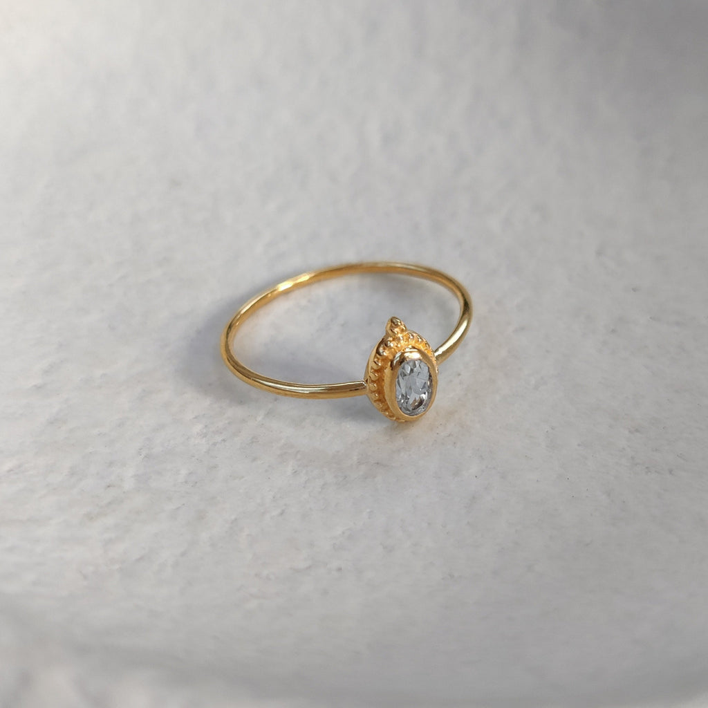 Gold ring with a small blue topaz gemstone on a textured white surface