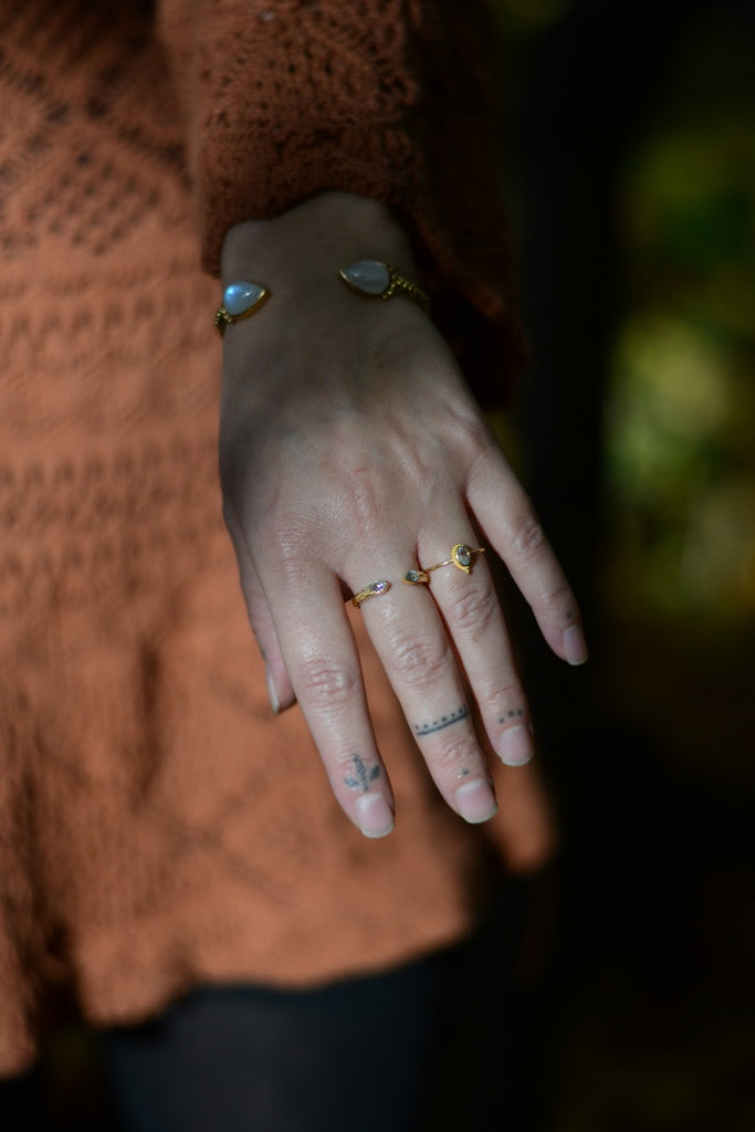 Hand with multiple gold rings  with blue topaz and a moonstone bracelet against a blurred background