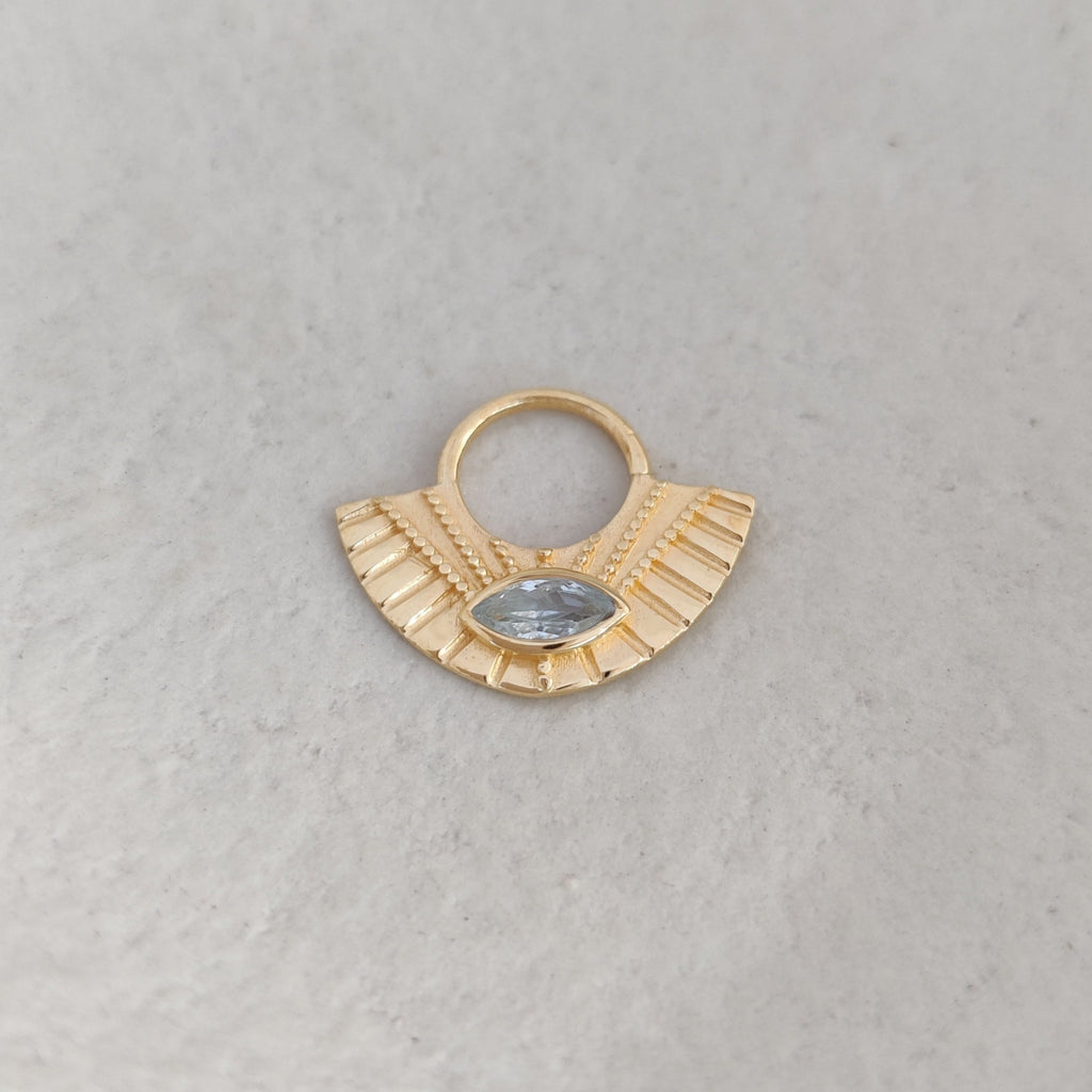 Gold fan-shaped earring with a small blue topaz gemstone on a light background.