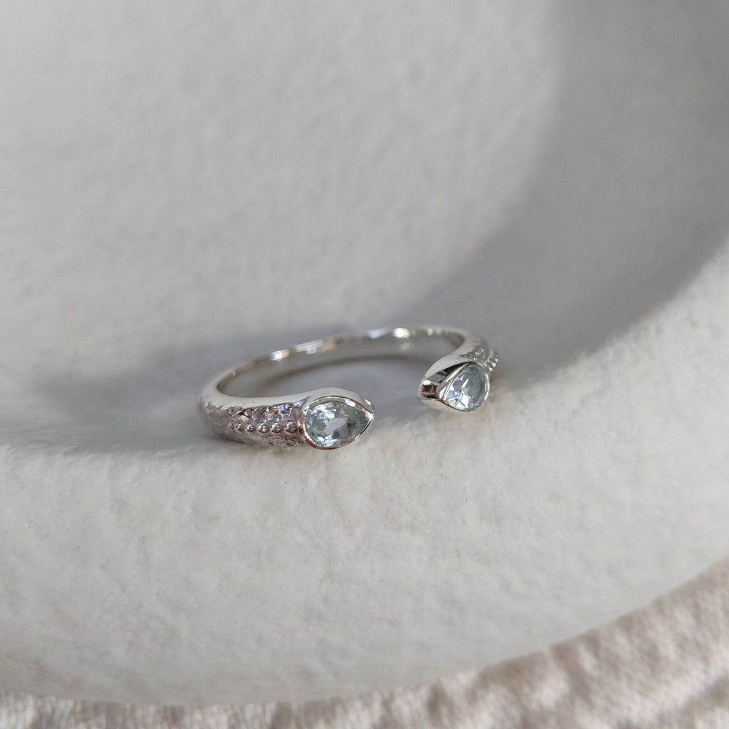 Silver ring with blue topaz gemstones on a textured white surface.