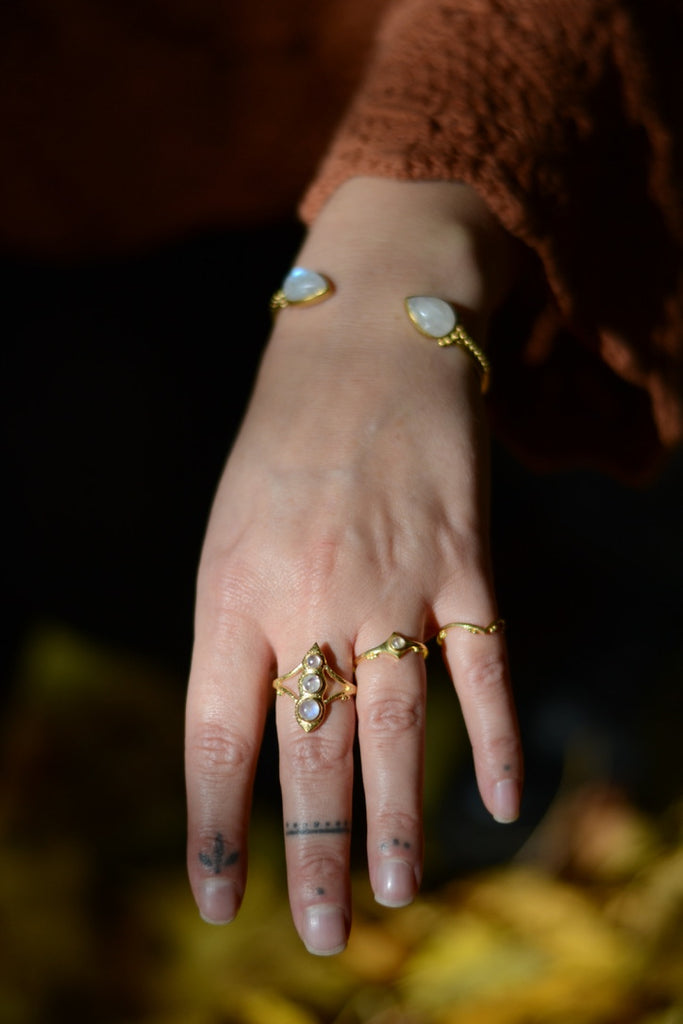 Hand wearing multiple gold rings with moonstones against a blurred natural background