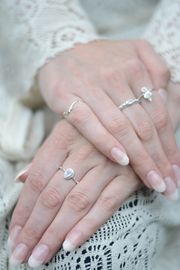 Close-up of hands wearing silver rings with moonstones on a textured fabric background.