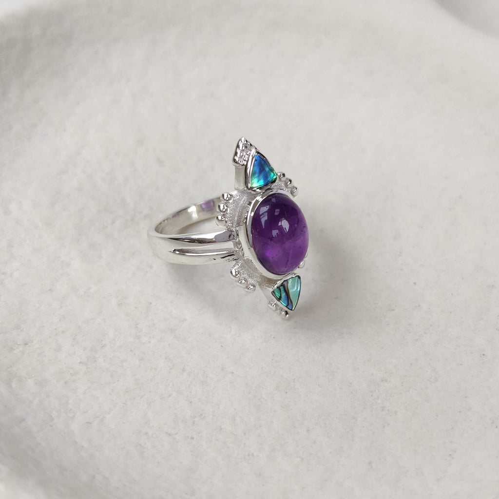Silver ring with a purple  amethyst gemstone on a white ceramic dish