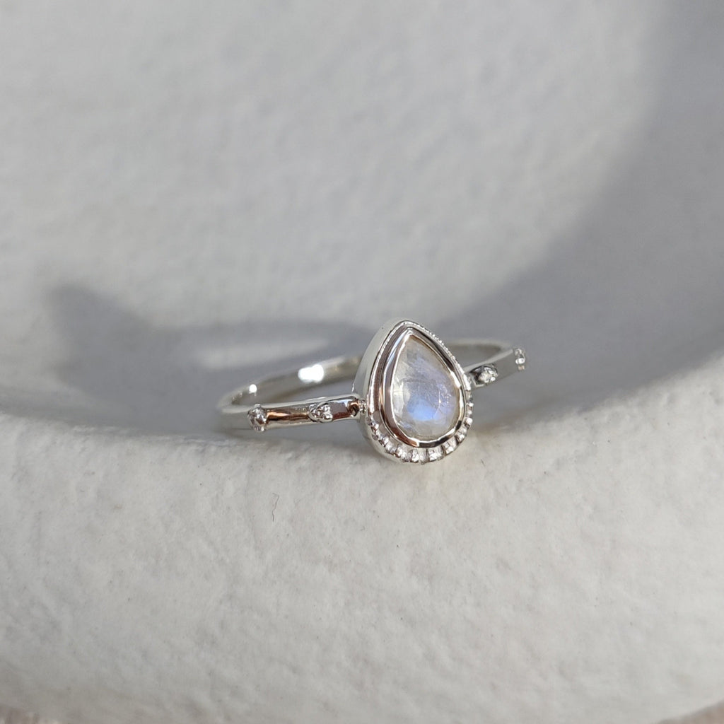 Silver ring with a drop-shaped moonstone on a textured white surface.