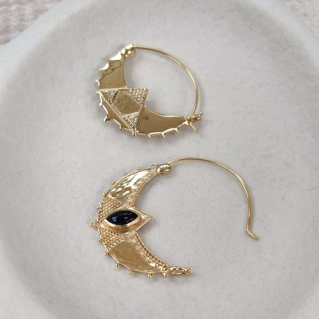 Gold earrings with black gemstones on a white textured surface. Displayed from front and back to show the unique design.