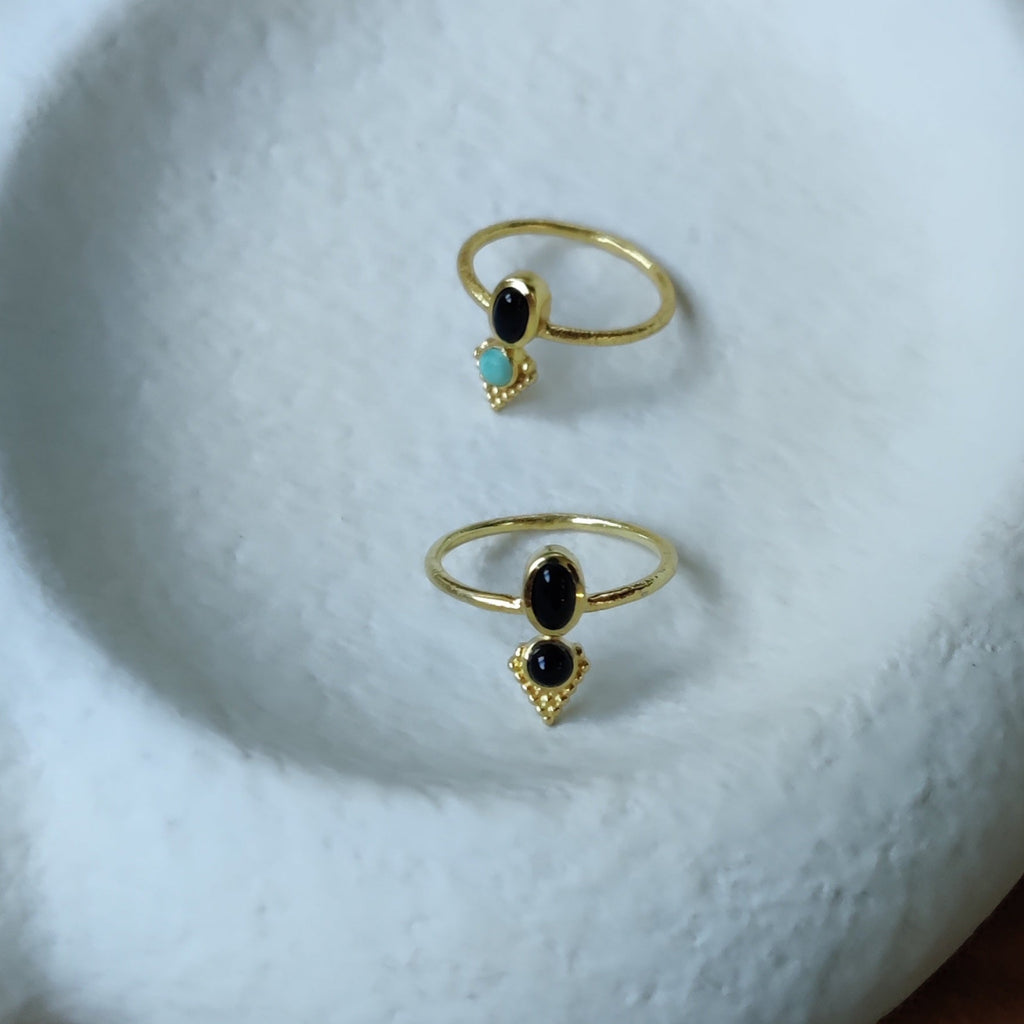 Dainty brass rings with turquoise and black onyx, displayed on a jewelry plate.