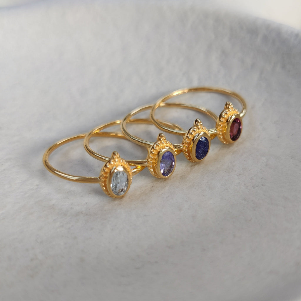 Four gold rings with different faceted gemstones on a white background.