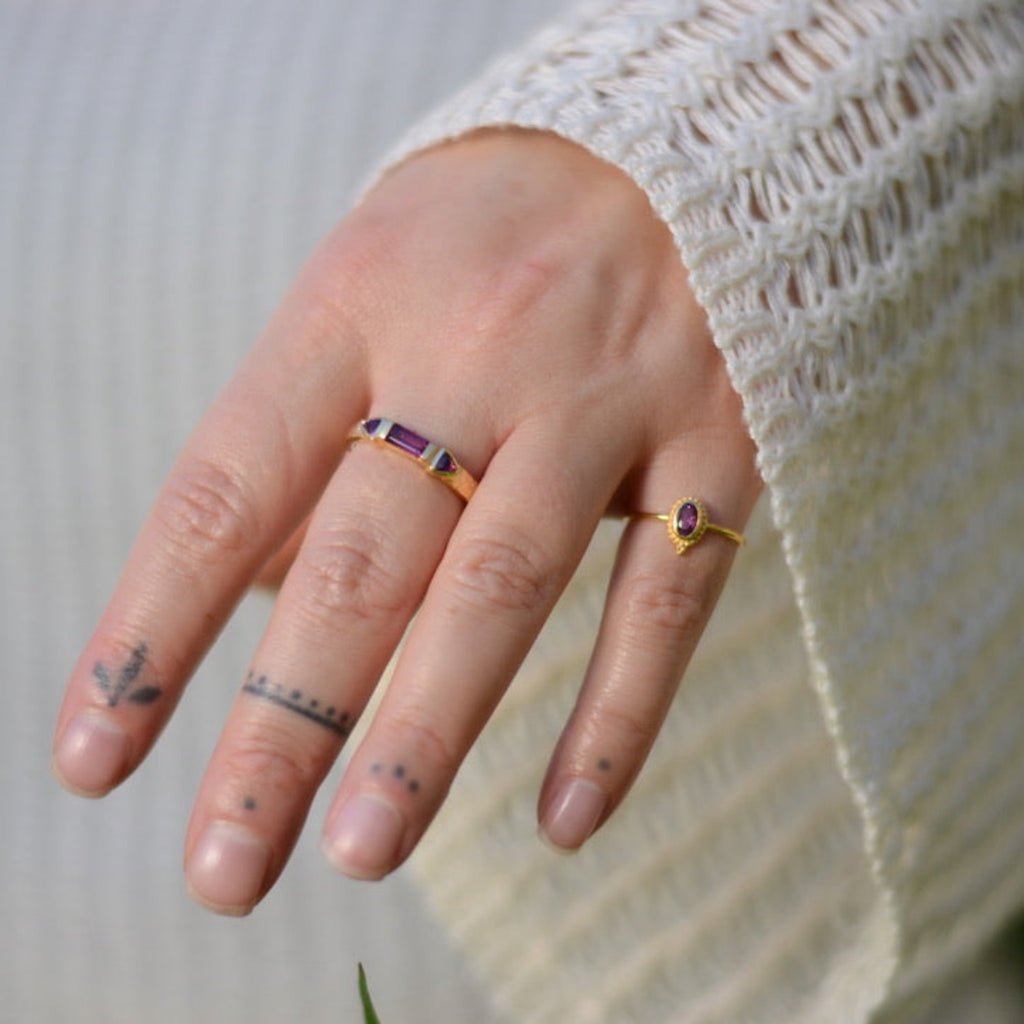 Close-up of a hand wearing two gold rings with red purple gemstones with a blurred background