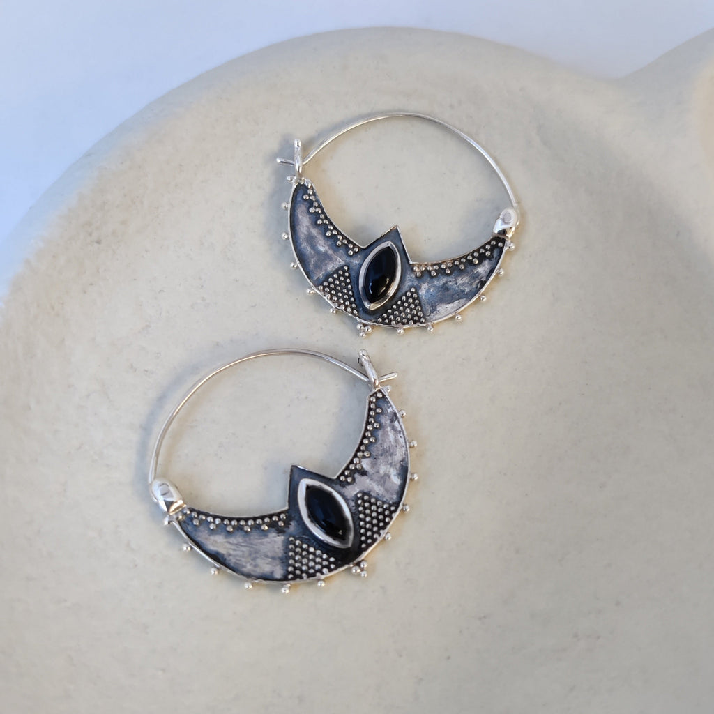 Close-up of silver crescent hoop earrings featuring black onyx, highlighting their intricate design.