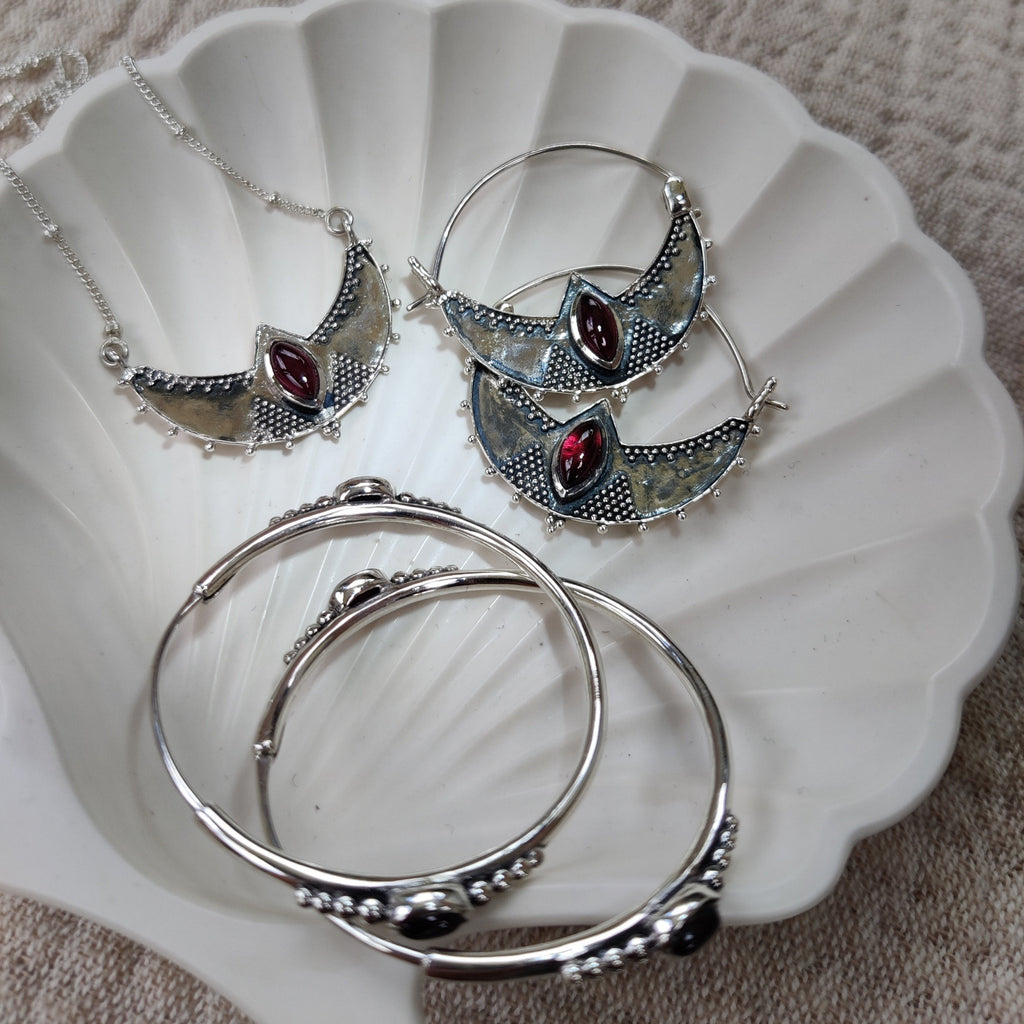 Silver earrings and necklace with garnet, displayed on a jewelry plate.