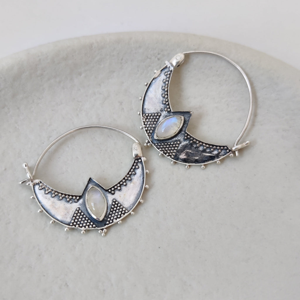 Close-up of silver crescent hoop earrings featuring shimmering moonstone, highlighting their intricate design and iridescent colors.