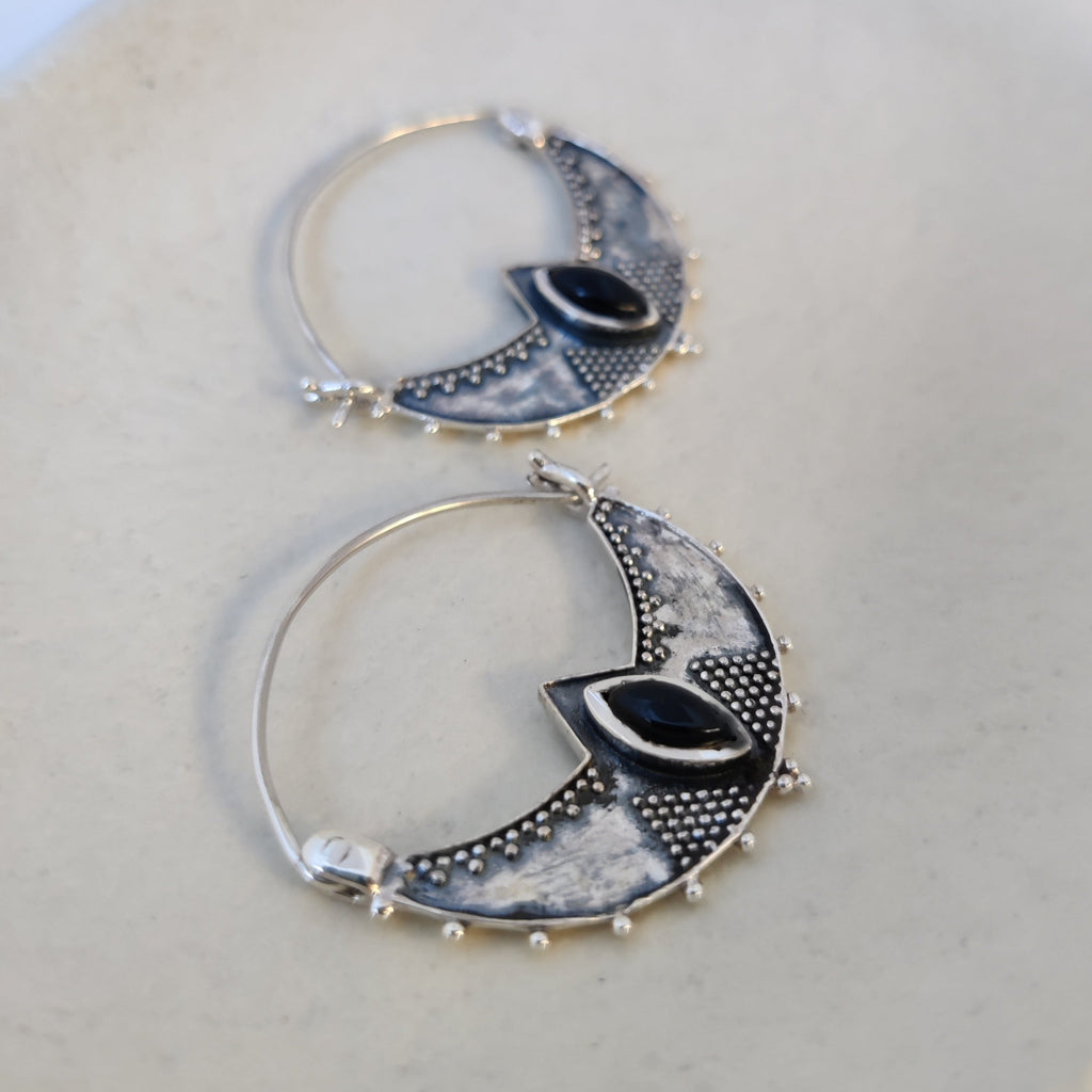 Close-up of silver crescent hoop earrings featuring black onyx, highlighting their intricate design.