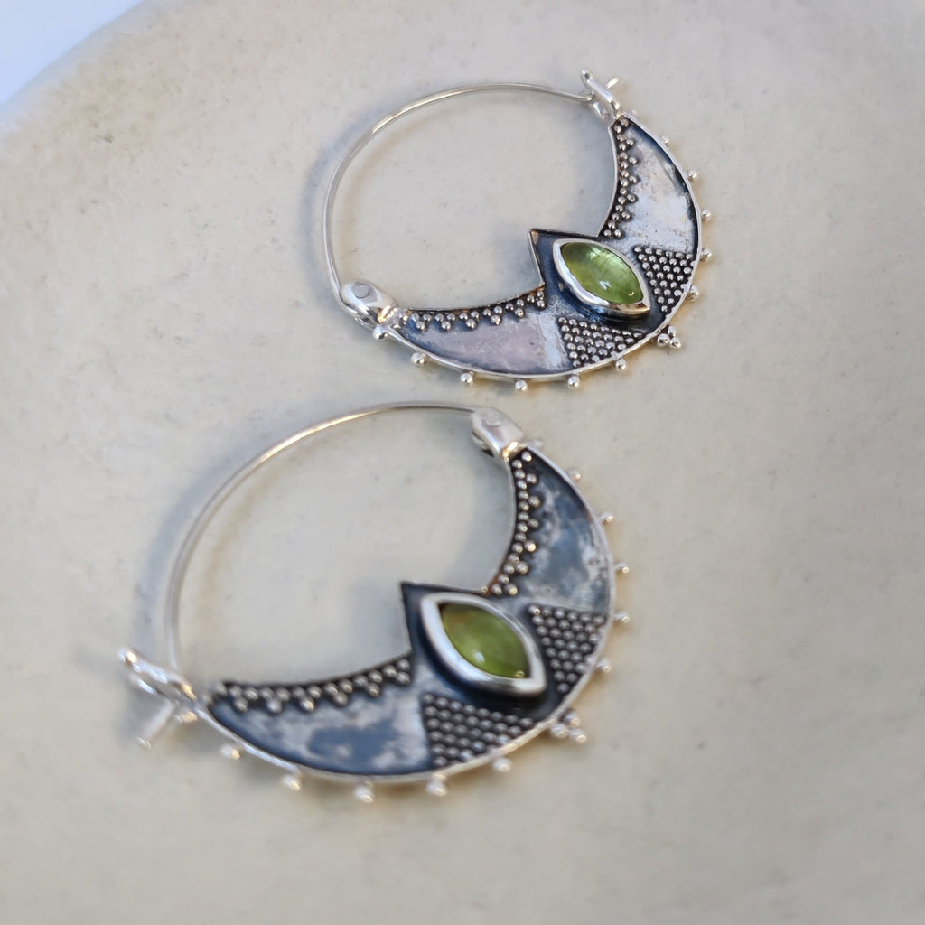 Close-up of silver crescent hoop earrings featuring peridot, highlighting their intricate design and vibrant green color.