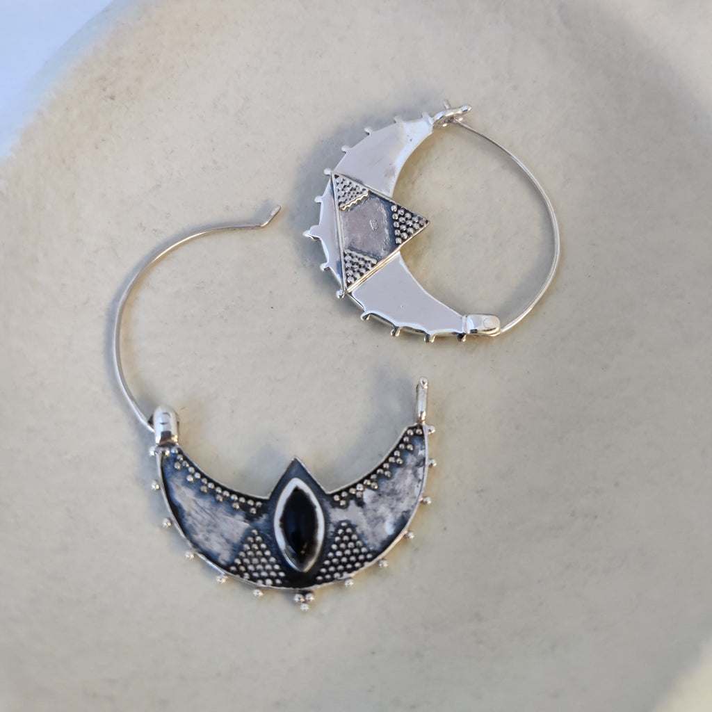 Close-up of silver crescent hoop earrings featuring black onyx, showcasing both the front and back sides, highlighting their intricate design and open closure mechanism.