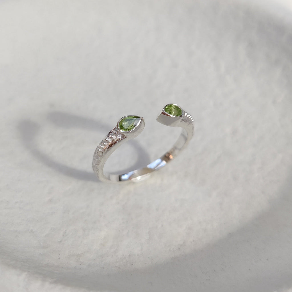 Open cuff silver ring with green gemstones on a white textured surface