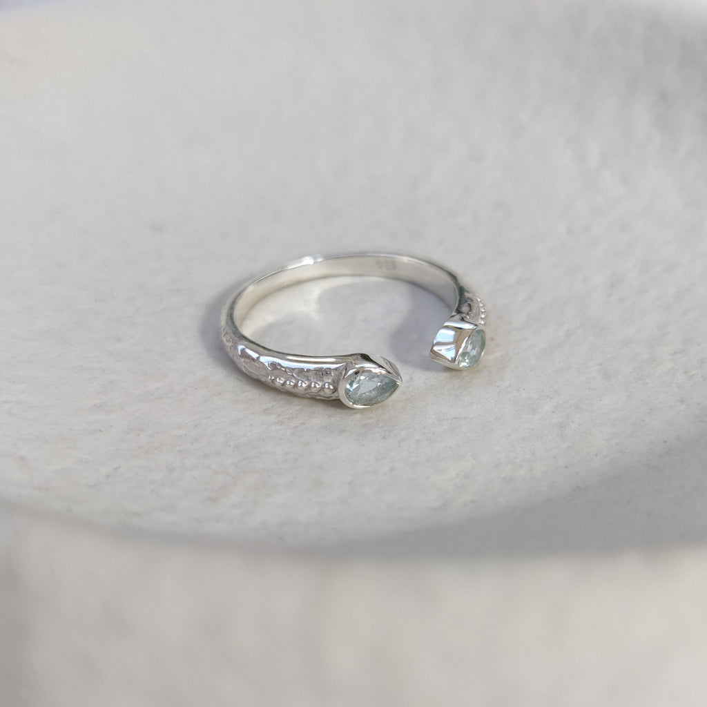 Open cuff silver ring with blue topaz gemstones on a white surface.