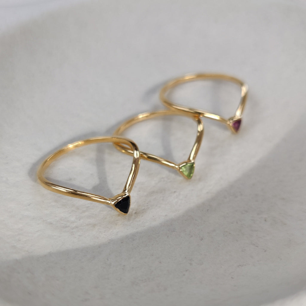 Gold rings with tiny trillion-shaped gemstones on a light background.