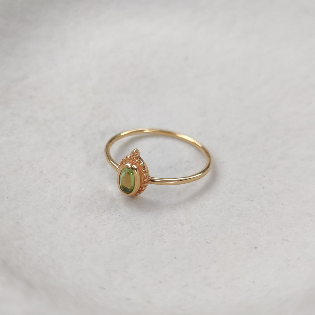 Gold ring with a green gemstone on a white surface.