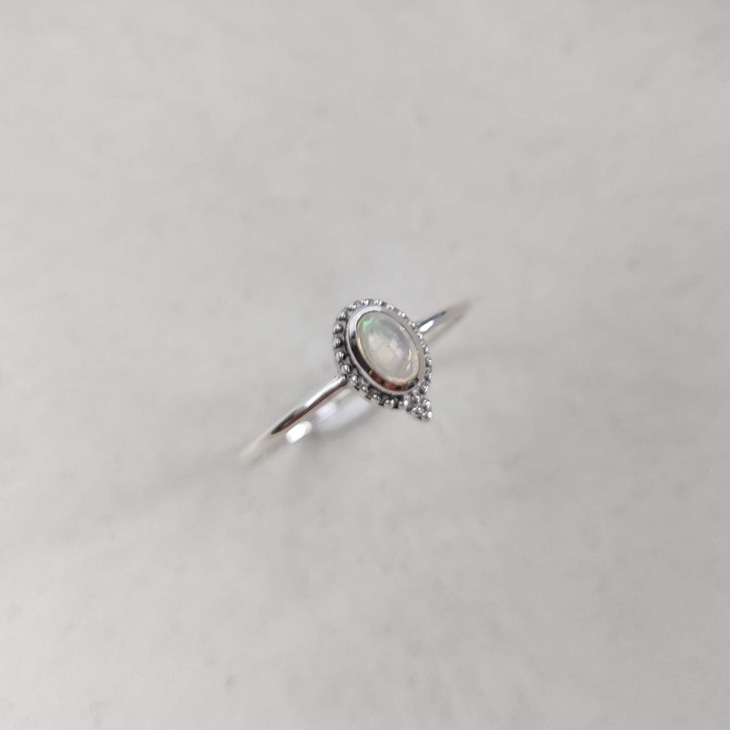 Silver ring with a central opal gemstone on a textured white surface.