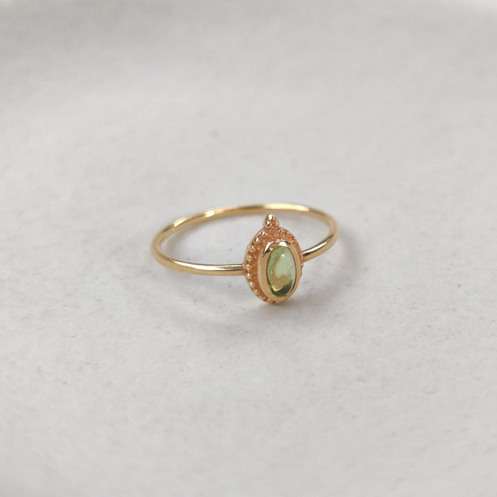 Gold ring with a green gemstone on a white surface