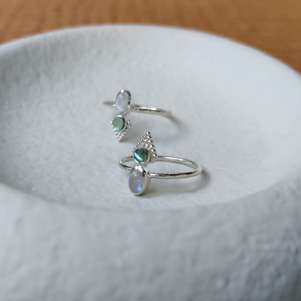 Small moonstone and abalone shell silver rings on a jewelry dish.