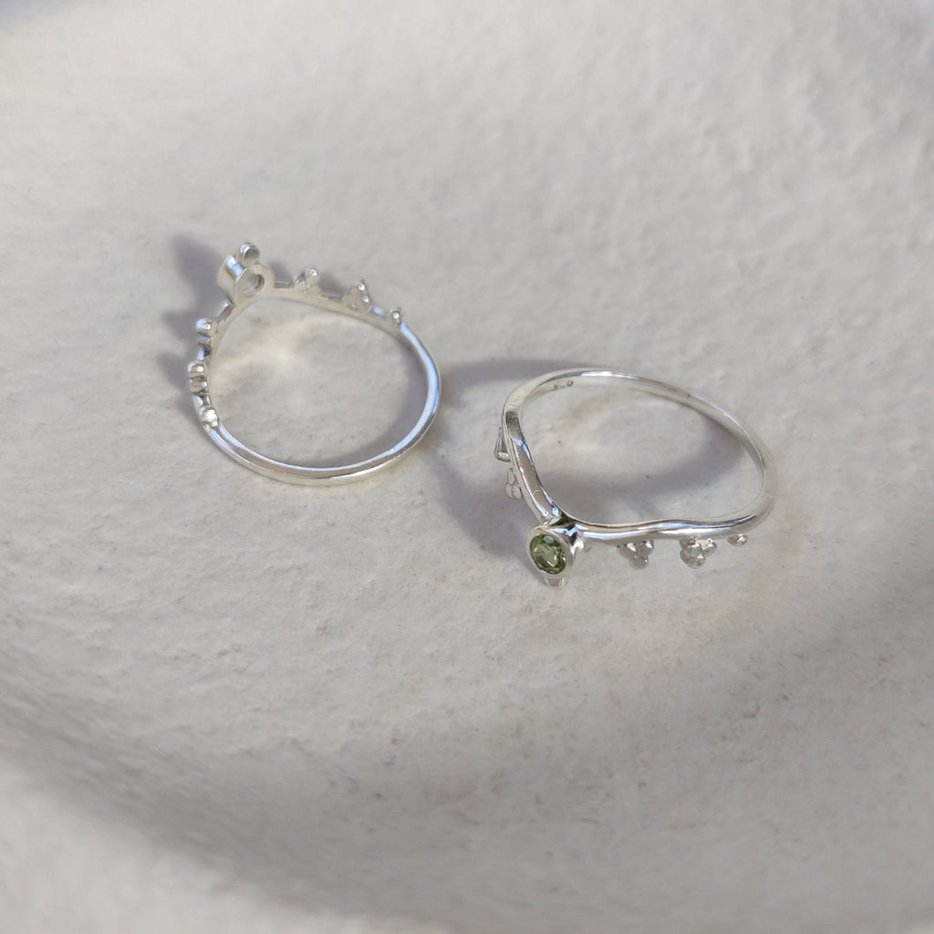 Silver stacking rings with green gemstones on a textured white surface.