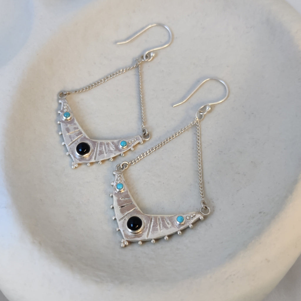 Dangling silver earrings with black onyx and turquoise, displayed on a jewelry plate.