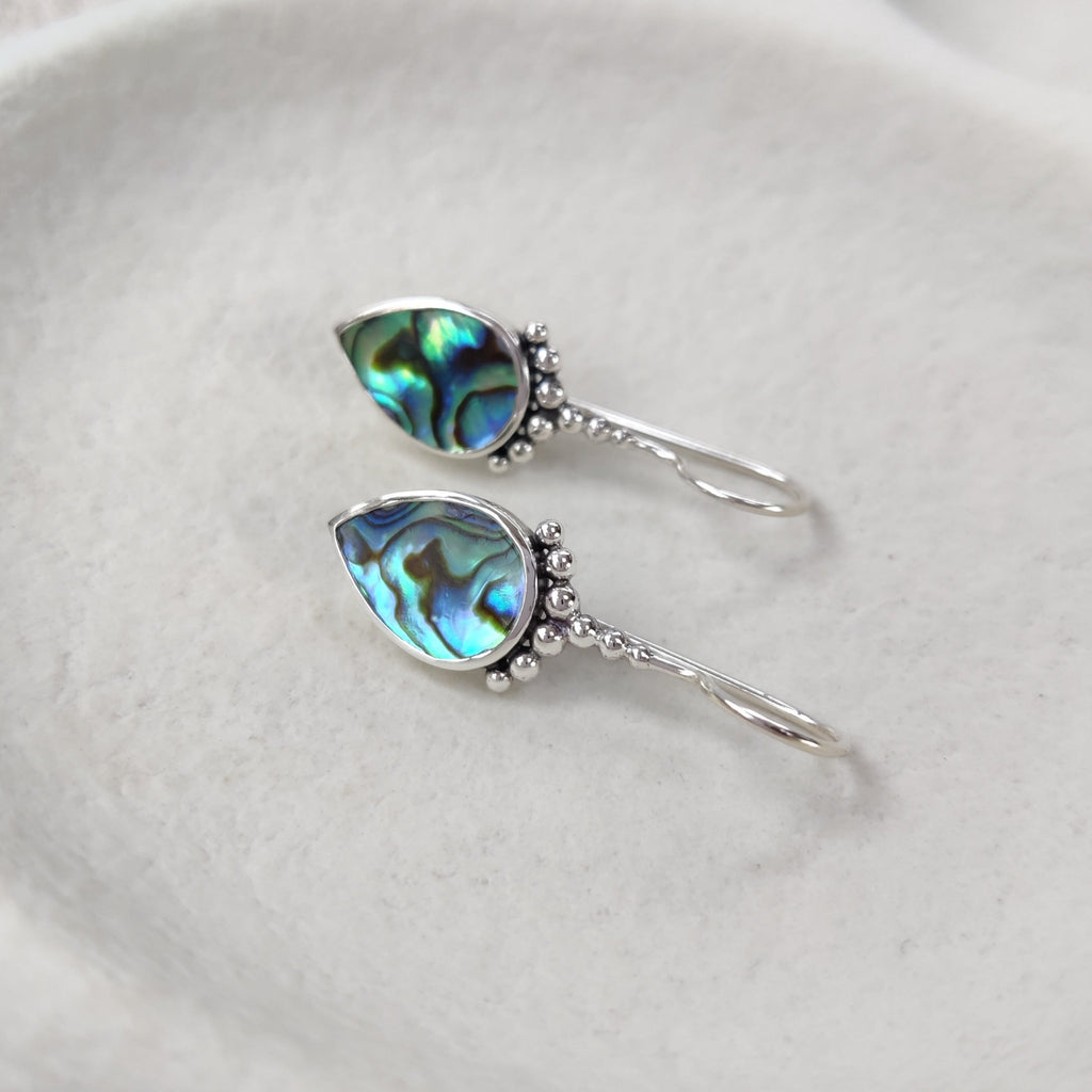 Pair of silver earrings with abalone shell on a white textured surface.
