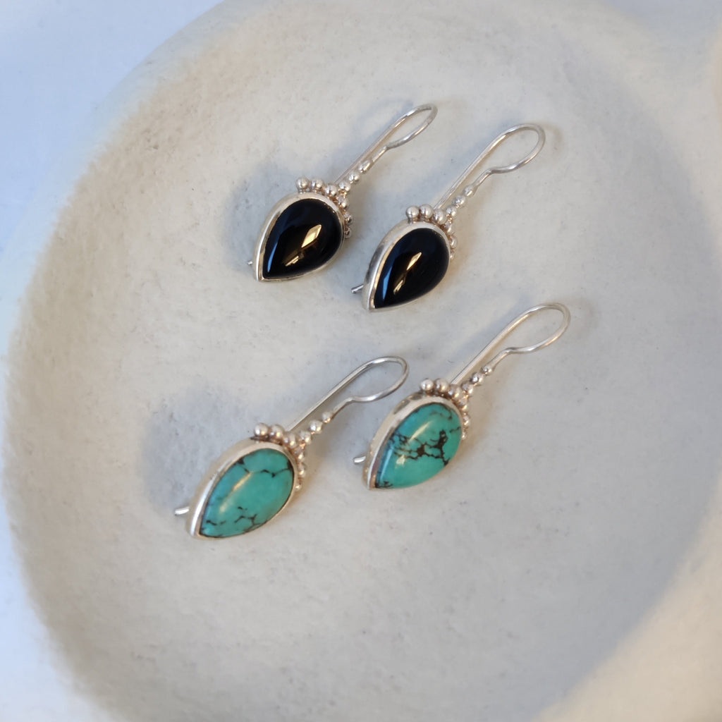 Silver drop earrings with black onyx and turquoise, displayed on a jewelry plate.
