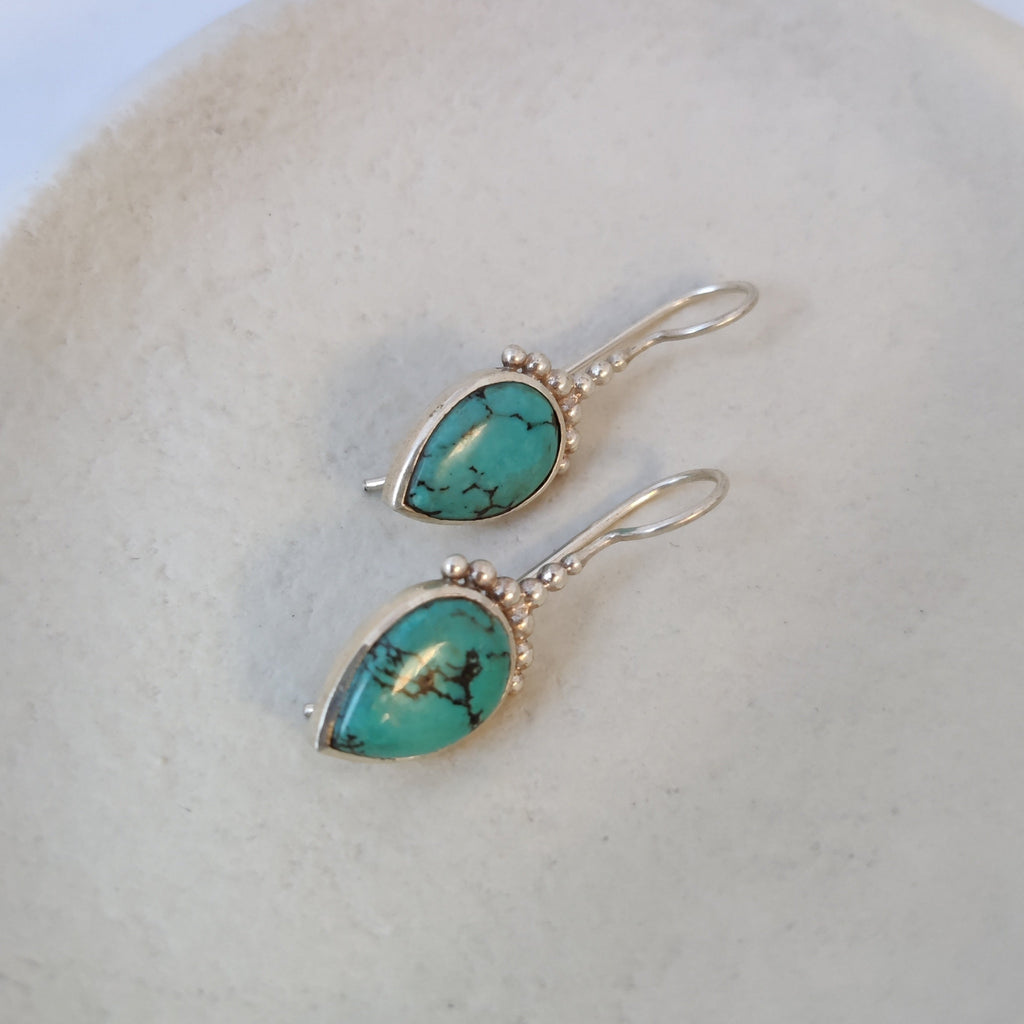 Drop silver earrings with turquoise, displayed on a jewelry plate.
