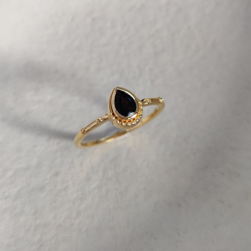 Drop-shaped gold ring with a black gemstone on a textured white surface