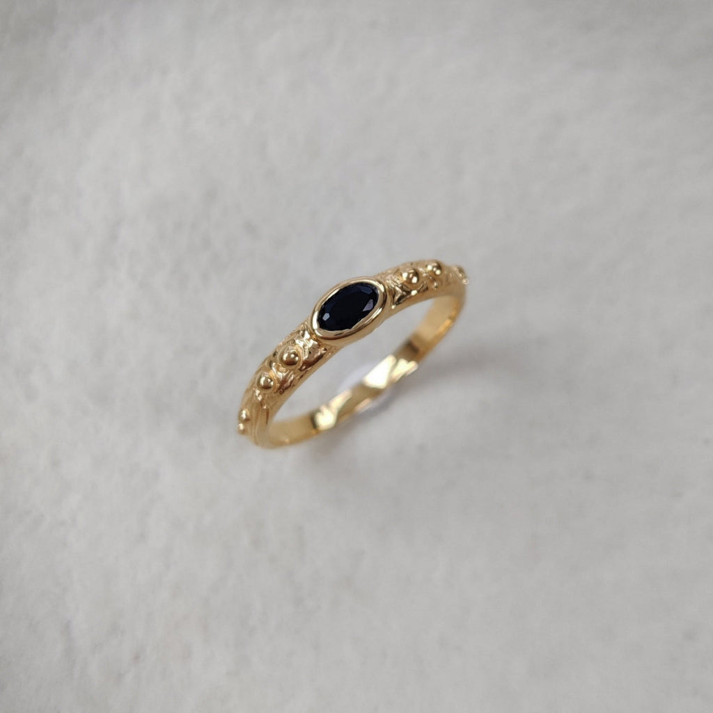 Gold ring with a black gemstone on a textured white surface.
