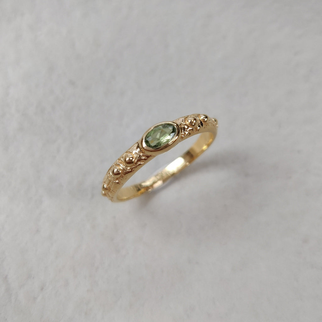 Gold ring with a green gemstone on a white surface.