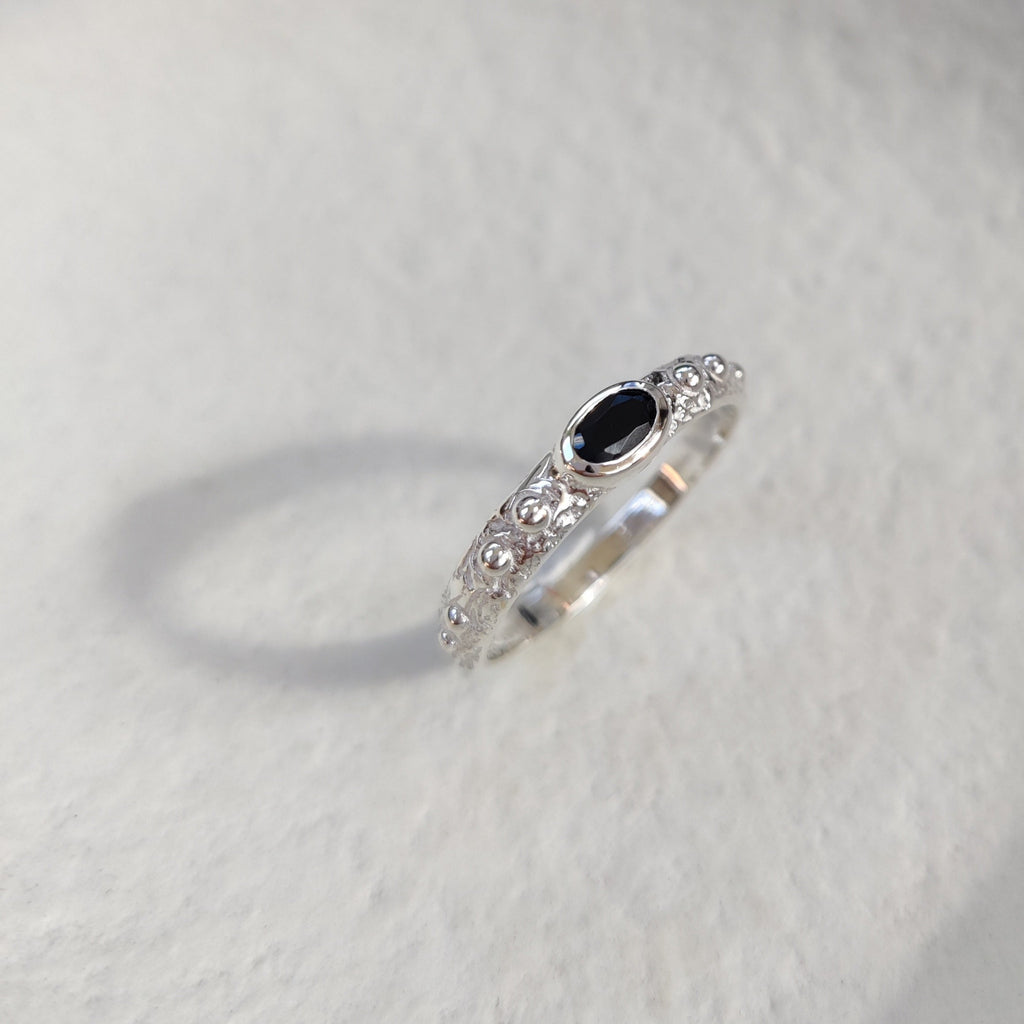 Textured silver ring with a black gemstone on a white surface.