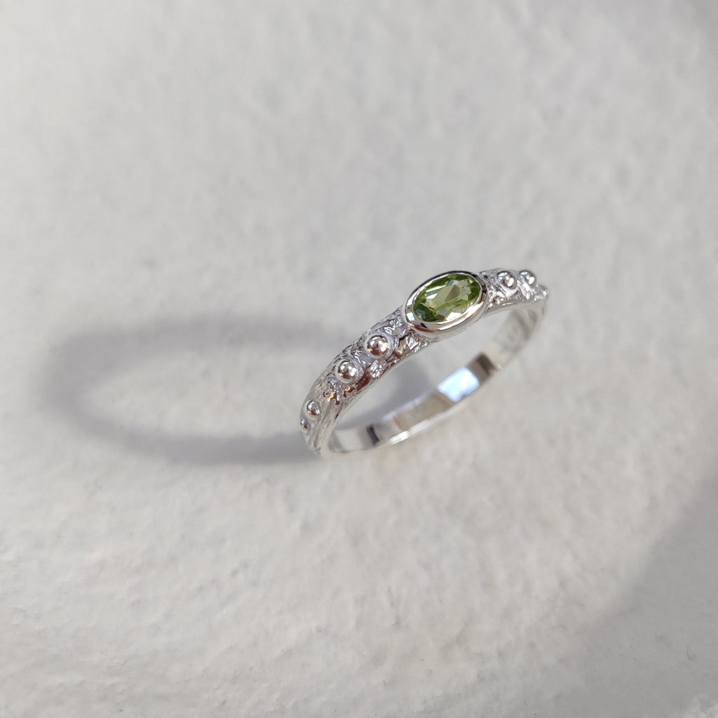 Textured silver ring with a green gemstone on a white background.