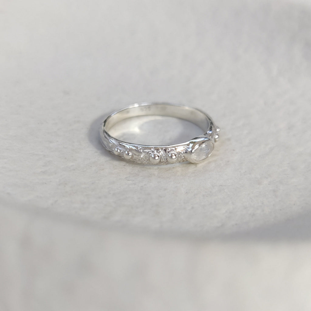 Textured silver ring with a small moonstone on a white background.